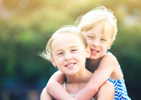 Two smiling little girls embracing each other in summer parkの写真素材