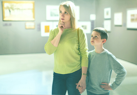 smiling russian young mother and son looking at paintings in halls of museumの写真素材