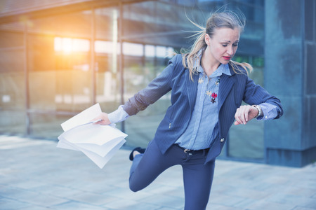 Businesswoman hurrying to meeting and watching on wristwatch outdoorsの写真素材