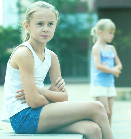 Two offended little girls not talking to each other after quarrel outdoorsの写真素材