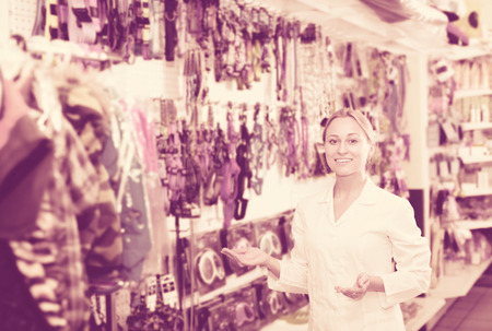 Pretty female shop assistant showing leashes for pets in pet shopの写真素材