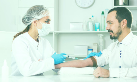 Young female nurse ready to make injection to male visitor in hospitalの写真素材