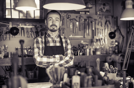 Serious male worker demonstrating his workplace and tools in leather workshopの写真素材