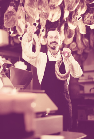Young russian male seller offering sausages in butchers shopの写真素材