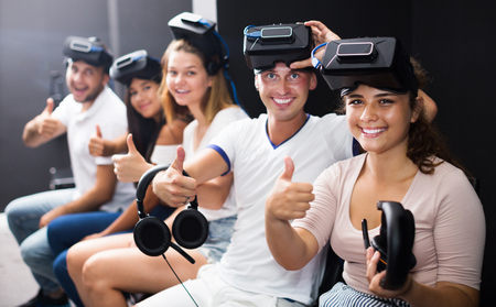 Smiling young people expressing satisfaction with vr attraction showing thumbs upの写真素材