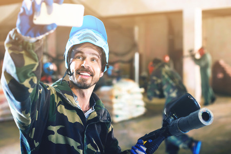 Young man in blue mask is making selfie on battlefield of paintball club.の写真素材