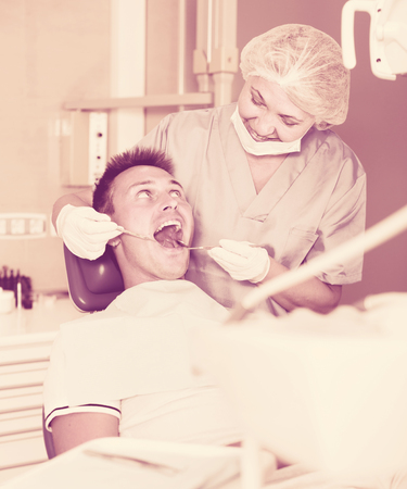 Female dentist with male patient during oral checkup in dentistryの写真素材