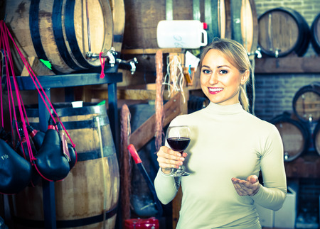 Portrait of cheerful  smiling female customer holding wine glass in wineryの写真素材