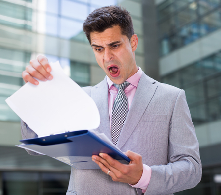 Businessman reading papers outdoor near large factory with shocked facial expressionの写真素材
