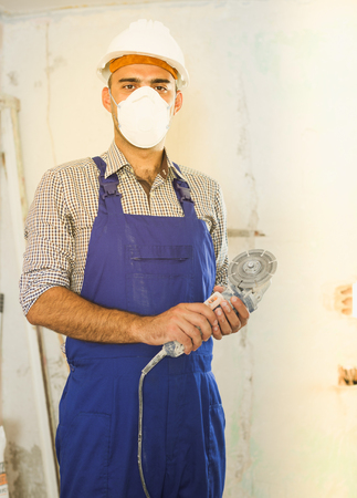 Portrait of positive worker repairer standing with electric saw in maskの写真素材