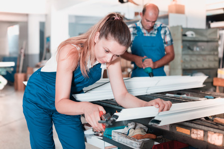Young diligent female worker cutting metal-plastic profiles in workshop, using nippersの写真素材