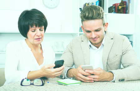 Cheerful mature mother with her handsome son studing new functions of smartphonesの写真素材