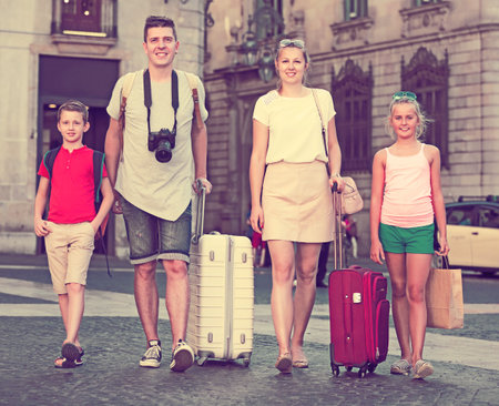 Young glad family of travelers with two children walking around city with suitcasesの写真素材