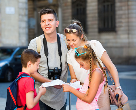 Cheerful positive parents with two kids traveling together searching location on paper mapの写真素材