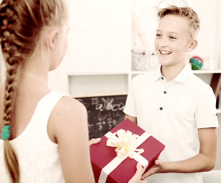 Girl is giveing a gift to friend on his birthday at home.の写真素材