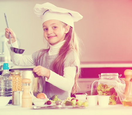 Little female chef preparing vegetable soup in kitchenの写真素材