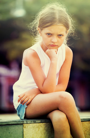 Lonely girl in elementary school age crying and feeling confused outdoorsの写真素材