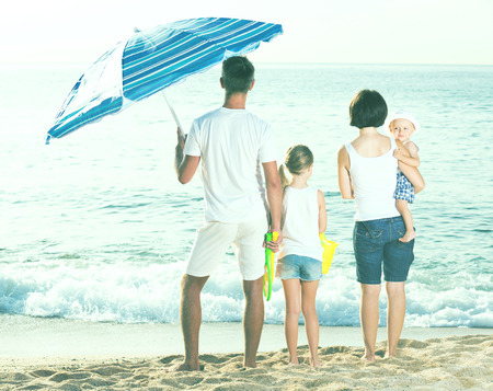 Family standing with back forward at beach on sunny summer dayの写真素材