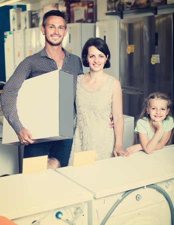 happy couple with girl shopping new electronics and holding box in storeの写真素材