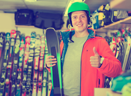 Portrait of client man in helmet and jacket who is standing with ski in sport shop.の写真素材