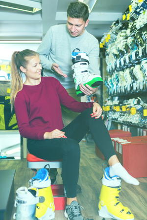 Salesman is helping woman to trying on boots for skiing in sport store.の写真素材