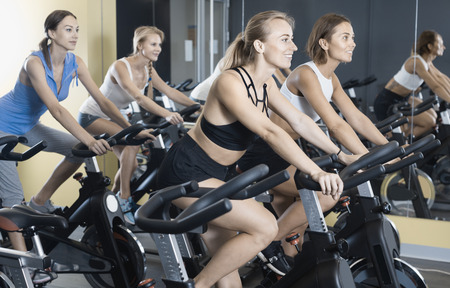 Athletic  positive  young girls during workout on stationary bicycle in fitness gymの写真素材