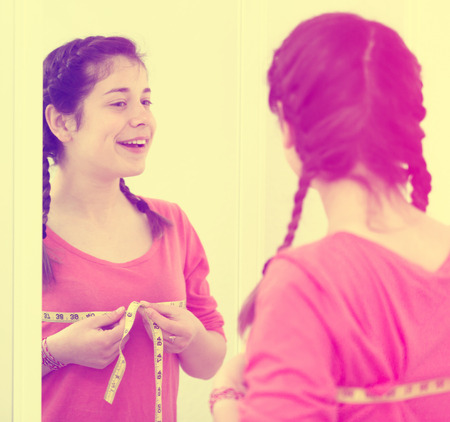 Young girl feeling happy measuring her breast at homeの写真素材