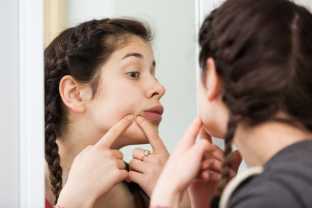 Female teenager squeezing acne spots alone at homeの写真素材
