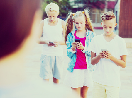 Modern serious kids spending time together outdoors using mobile gadgetsの写真素材