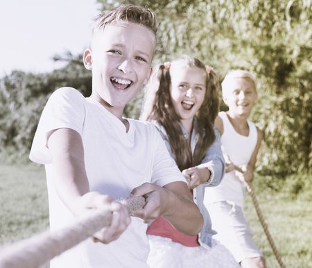 Children playing tug of war during joint games outdoors on sunny dayの写真素材