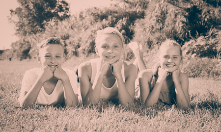 Cheerful girl with two friends  resting after game on green grassの写真素材