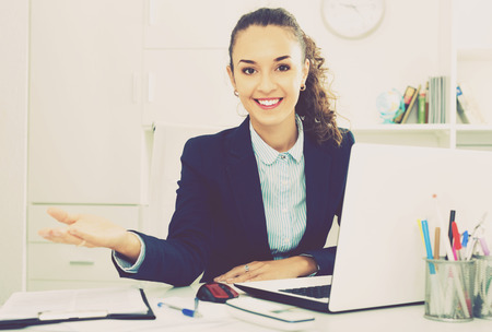 Cheerful smiling  business lady sitting at office desk with laptopの写真素材