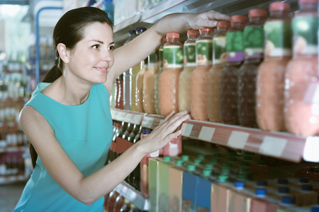 Young woman is holding bottle with juice in the shop.の写真素材