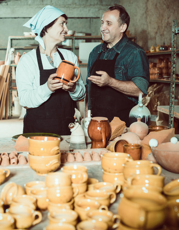 Portrait of positive elderly potters displaying cups at the workshopの写真素材