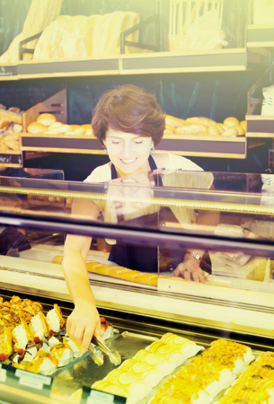 Senior female with tasty confectionery products on counter of bakeryの写真素材