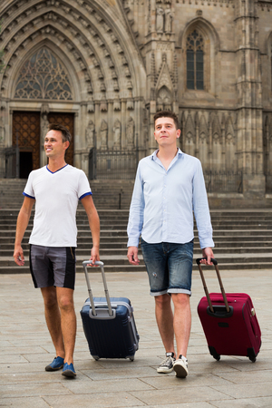 Men travelers with baggage heading to hotel on foot at vacationの写真素材