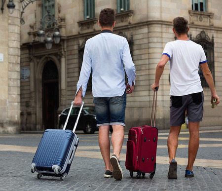 Rear view of cheerful positive men with baggage in streetの写真素材