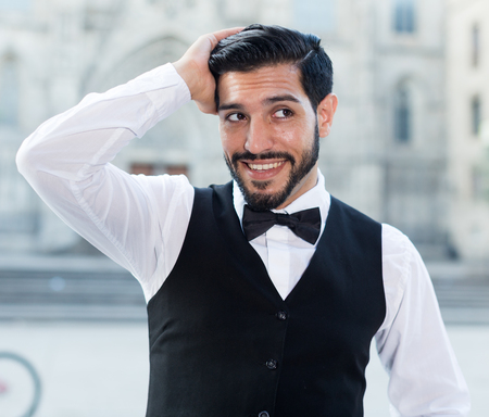 Handsome young man in formalwear adjusting his hairstyle and smiling standing outdoorsの写真素材