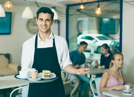 Smiling waiter holding served tray meeting visitors at pastry barの写真素材