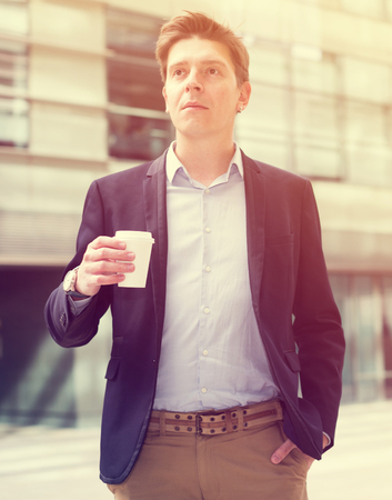 Professional man in jacket with coffee standing at the streetの写真素材