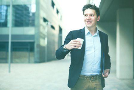 Portrait of cheerful male with documents standing outdoor drinking coffeeの写真素材