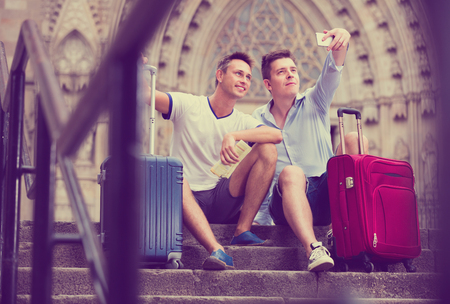 Two cheerful  guys with luggage  taking selfie in city at summer dayの写真素材