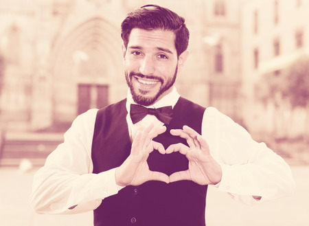 Happy smiling young man showing sign of heart with his fingersの写真素材