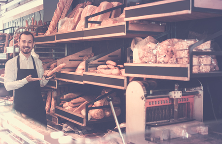happy germany male shop assistant demonstrating delicious loaves of bread in bakeryの写真素材