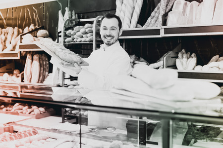Optimistic assistant demonstrating delicious festive cake in bakeryの写真素材