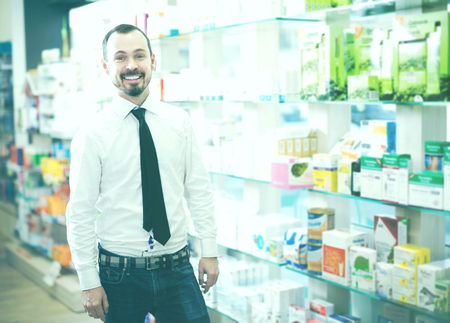 Smiling man customer browsing rows of drugs in drugstoreの写真素材