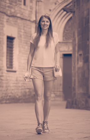 Attractive young woman in casuals walking along ancient streetの写真素材