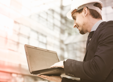Smiling professional man in jacket and helmet working at electonic device outdoorの写真素材