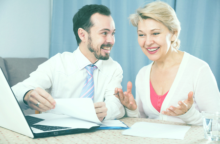Smiling mature female and sales manager discussing conditions of contract at homeの写真素材
