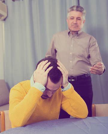 Mature father talking seriously and instructs his son at homeの写真素材